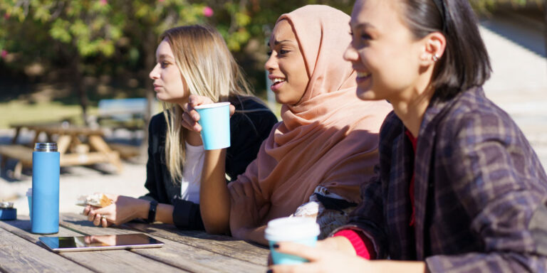 Three women sharing laughter and conversation in a sunny outdoor setting.